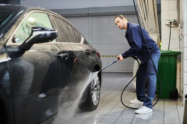 Handsome hard working professional in blue comfy uniform with collected hair washing black car — Stock Photo