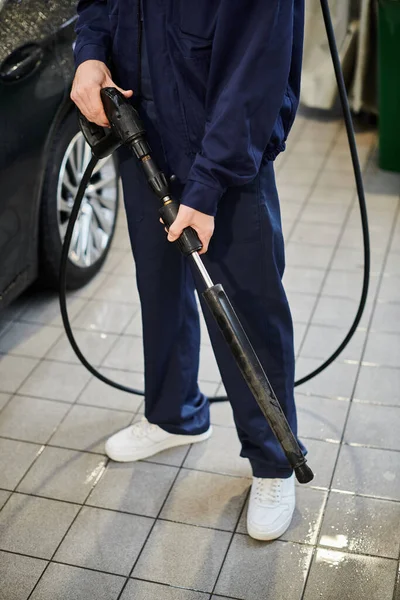 Vue recadrée du militaire travaillant dur en uniforme bleu se préparant à utiliser un tuyau pour laver la voiture noire — Photo de stock