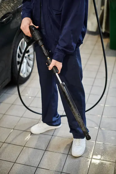Cropped view of hard working serviceman in blue uniform preparing to use hose to wash black car — Stock Photo