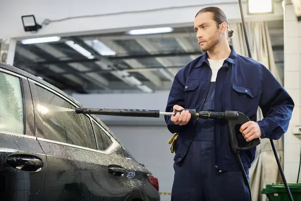 Good looking dedicated serviceman in blue comfy uniform with collected hair using hose to wash car — Stock Photo