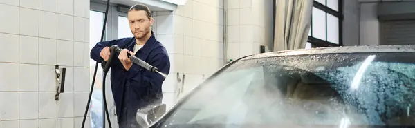 Handsome dedicated specialist in blue uniform with collected hair washing car in garage, banner — Stock Photo