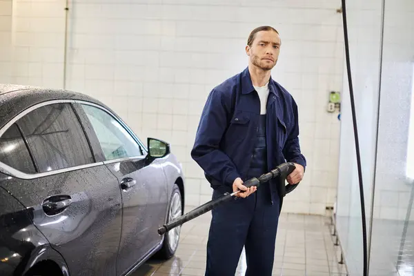 Handsome dedicated serviceman in uniform holding hose before washing car and looking at camera — Stock Photo