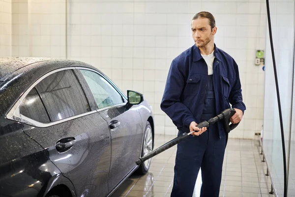 Attractive devoted professional in blue uniform with collected hair using hose to wash black car — Stock Photo