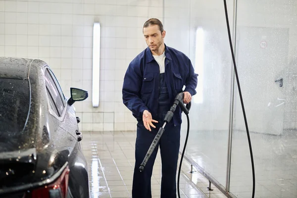Handsome hard working specialist in uniform with collected hair washing black car in garage — Stock Photo