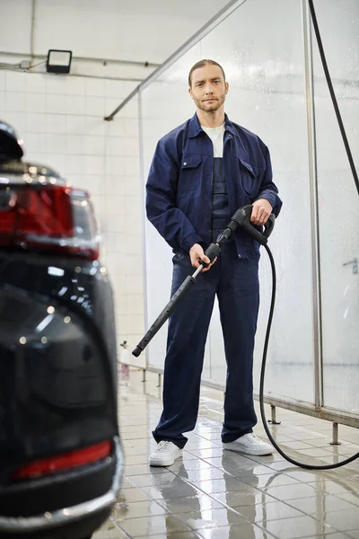 Joyous attractive serviceman in uniform holding hose preparing to wash car and smiling at camera — Stock Photo