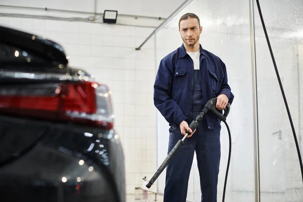 Joyous appealing professional worker in blue uniform preparing to use hose to wash car in garage — Stock Photo