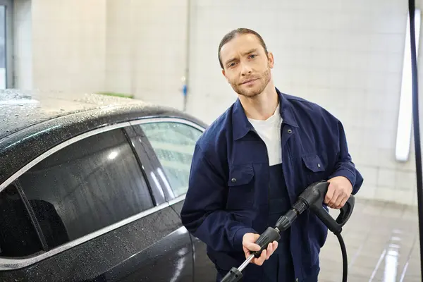 Cheerful handsome serviceman in uniform holding hose preparing to wash car and smiling at camera — Stock Photo