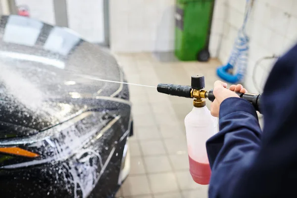 Visão recortada de trabalhador profissional dedicado em uniforme azul usando sabão para lavar carro moderno preto — Fotografia de Stock