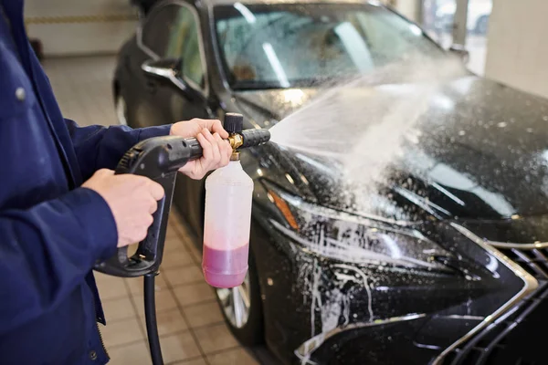 Abgeschnittene Ansicht von engagierten hart arbeitenden Spezialisten in blauer Uniform mit Seife, um schwarzes Auto zu waschen — Stockfoto