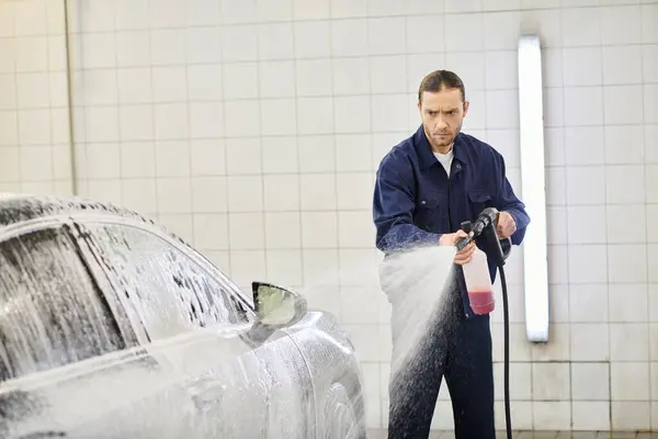 Schöner hart arbeitender Profi in bequemer Uniform mit Seife, um schwarzes Auto in der Garage zu waschen — Stockfoto