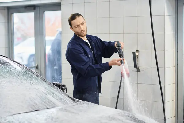 Handsome hard working serviceman with collected hair in uniform washing black car with soap — Stock Photo