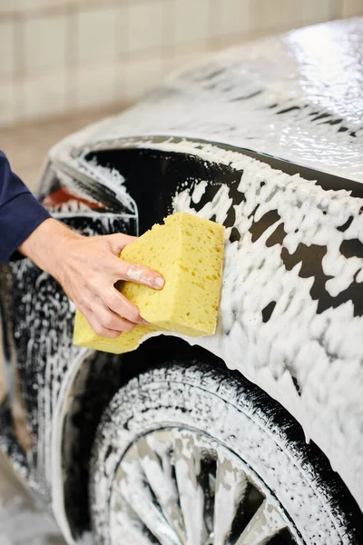 Cropped view of hard working dedicated specialist in uniform washing black car using sponge — Stock Photo