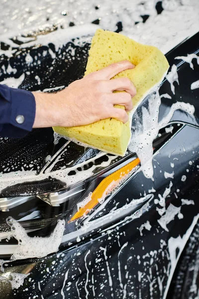 Cropped view of dedicated specialist in blue uniform using soapy sponge to wash black modern car — Stock Photo