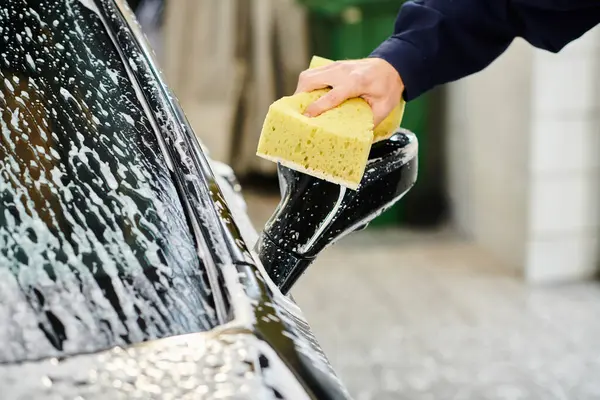 Cropped view of hard working professional serviceman in uniform using sponge to wash car in garage — Stock Photo