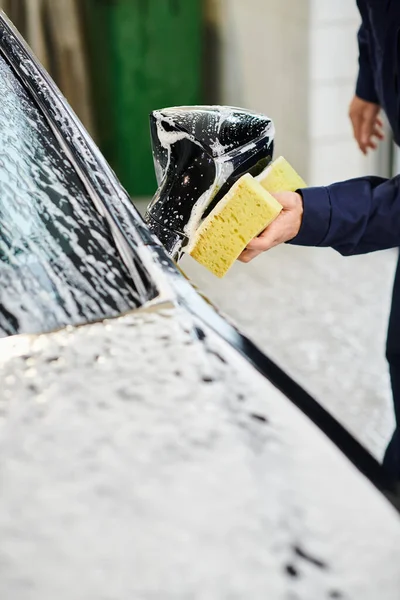 Cropped view of devoted hard working specialist in comfy uniform washing car with soapy sponge — Stock Photo