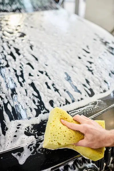 Cropped view of devoted hard working serviceman in uniform washing black modern car with sponge — Stock Photo