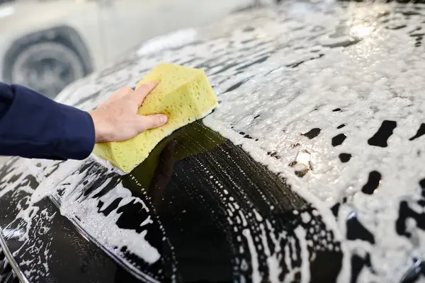 Обрізаний вид спеціального професійного працівника в синій формі з використанням губки для миття чорного автомобіля — стокове фото