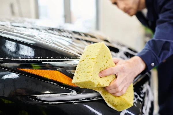 Focus on soapy yellow sponge in hands of blurred attractive serviceman washing black modern car — Stock Photo