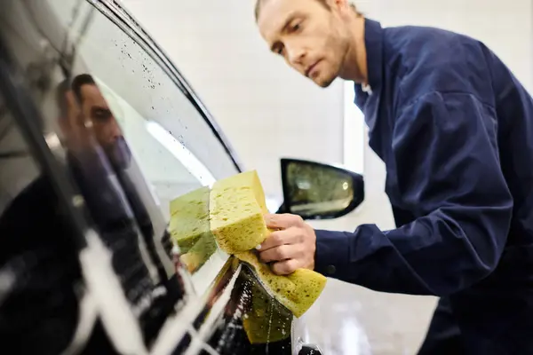 Se concentrer sur l'éponge savonneuse dans les mains d'un spécialiste du travail dur flou dans la voiture de lavage uniforme bleu — Photo de stock