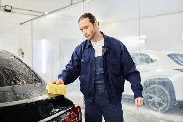 Appealing enthusiastic serviceman in blue uniform with collected hair washing car with sponge — Stock Photo