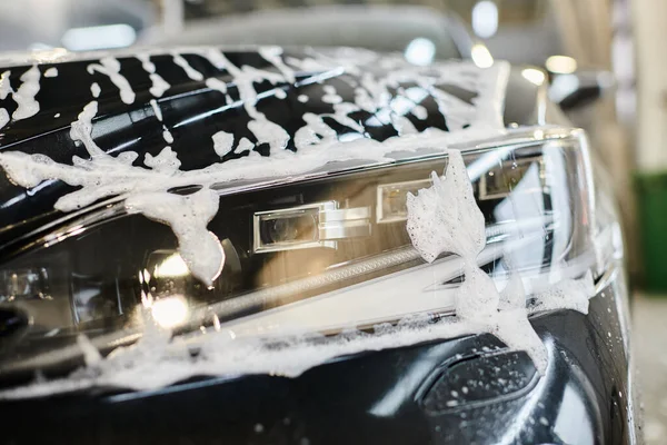 Об'єктна фотографія фари чорного сучасного автомобіля, покритого милом під час миття в гаражі — стокове фото