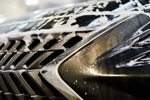 Объектное фото блестящего бампера черного современного автомобиля, покрытого мылом в процессе автодетализации — стоковое фото