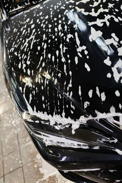 Об'єктна фотографія блискучого і мильного чорного сучасного автомобіля під час служби деталізації автомобіля в гаражі — стокове фото