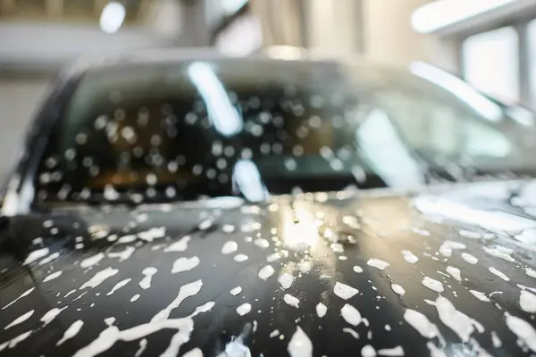 Object photo of soapy hood of black modern automobile during car detailing service in garage — Stock Photo