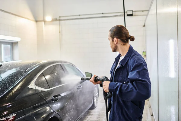 Schöner professioneller Servicemann in blauer bequemer Uniform wäscht schwarzes Auto sorgfältig in der Garage — Stockfoto
