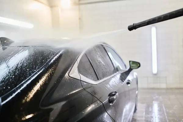 Cropped view of enthusiastic dedicated serviceman washing black modern car attentively in garage — Stock Photo