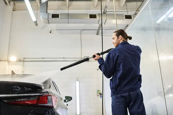 Good looking dedicated professional in uniform with collected hair using hose to wash black car — Stock Photo