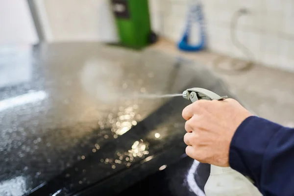 Visão cortada de trabalhador profissional dedicado usando pulverizador com água para limpar carro preto — Fotografia de Stock