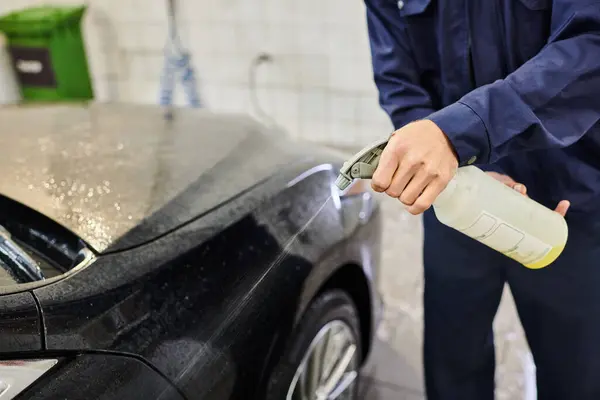 Vista cortada de serviceman dedicado usando pulverizador com água para limpar carro moderno preto na garagem — Fotografia de Stock