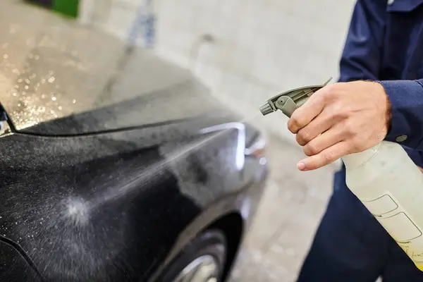 Cropped view of hard working professional in uniform using pulverizer to clean black modern car — Stock Photo
