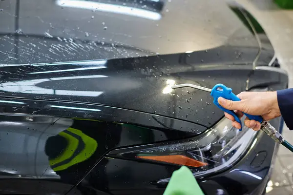 Cropped view of devoted professional worker in uniform cleaning car with water hose and rag — Stock Photo