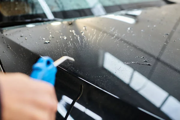 Cropped view of dedicated serviceman in uniform using water hose to clean black modern car — Stock Photo