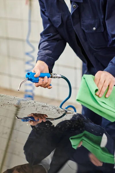 Ausgeschnittene Ansicht eines hart arbeitenden Berufssoldaten in blauer Uniform, der Lappen und Schlauch benutzt, um sein Auto zu reinigen — Stockfoto