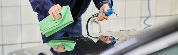 Cropped view of dedicated hard working specialist in uniform using hose and rag to clean car — Stock Photo