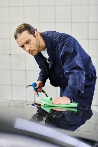 Appealing hard working specialist in blue comfy uniform using hose and rag to clean black car — Stock Photo