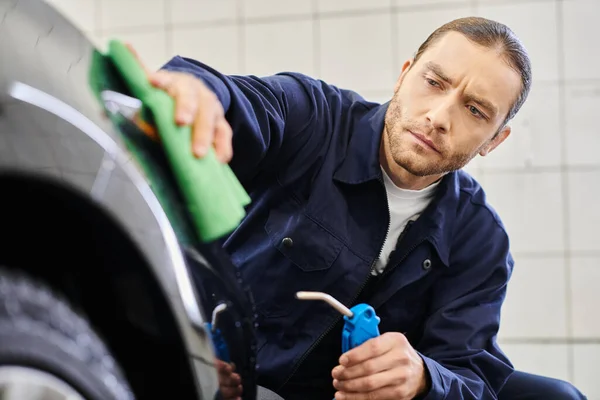 Attractive dedicated professional with collected hair in uniform using hose and rag to clean car — Stock Photo