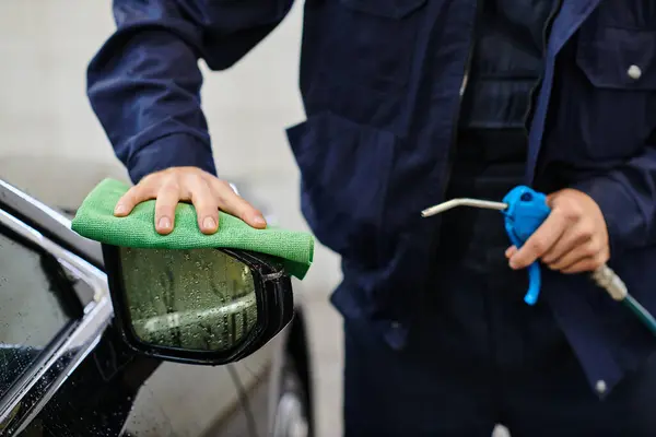 Cropped view of dedicated serviceman in blue uniform cleaning car using hose and rag in garage — Stock Photo