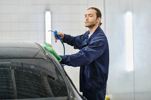 Handsome hard working serviceman in uniform with collected hair cleaning attentively black car — Stock Photo