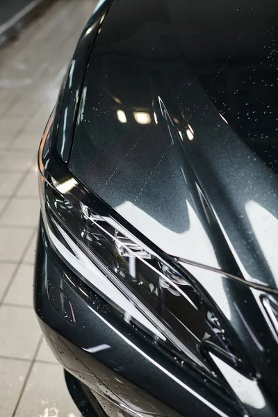 Об'єктна фотографія чорного сучасного автомобіля та його фари припарковані в гаражі під час миття — стокове фото