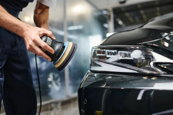 Cropped view of dedicated hard working professional in uniform using polishing machine on black car — Stock Photo