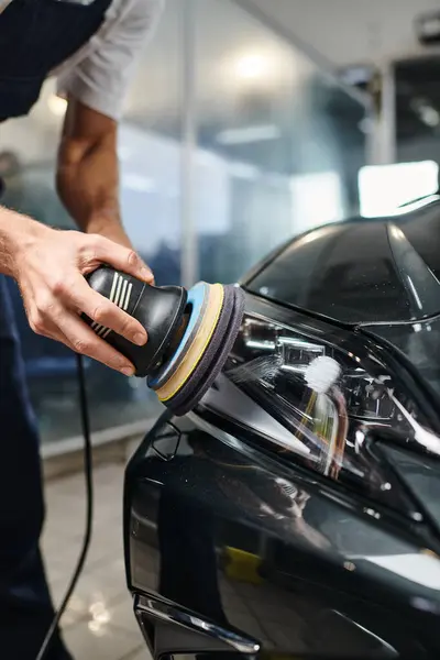 Cropped view of devoted professional worker in uniform using polishing machine on black car — Stock Photo