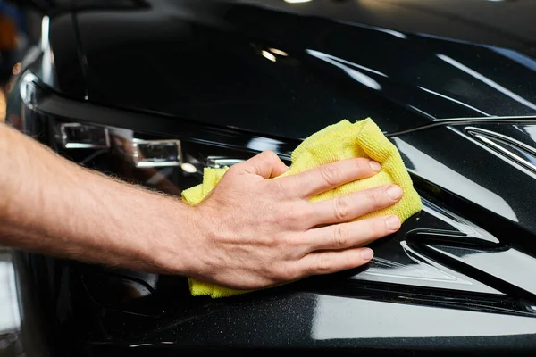 Cropped view of hard working professional serviceman using small rag to clean black modern car — Stock Photo