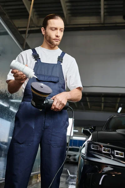 Bell'operaio in uniforme che applica la pasta sulla lucidatrice mentre è in garage — Foto stock