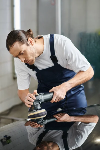 Beau travailleur dévoué avec les cheveux collectés en uniforme en utilisant la machine de polissage sur la voiture — Photo de stock