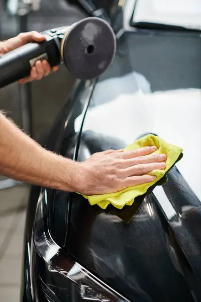 Cropped view of devoted professional serviceman cleaning car with rag and holding polishing machine — Stock Photo