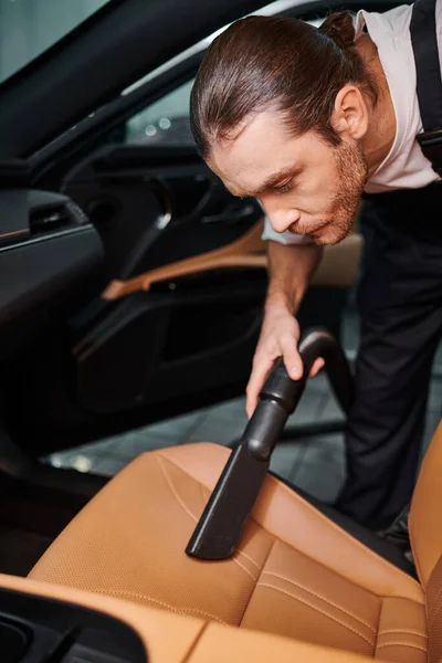 Bon travailleur regardant dur en uniforme en utilisant l'aspirateur manuel dans la voiture dans le garage — Photo de stock